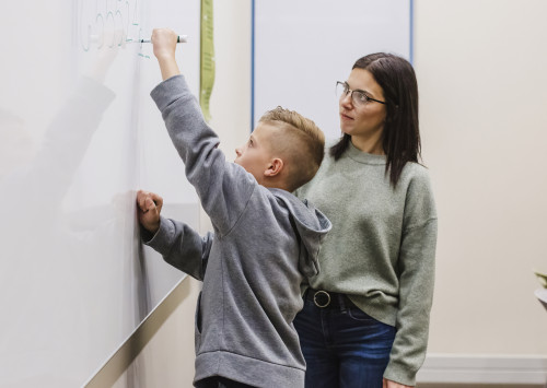 Therapist working with student who is writing on a white erase board